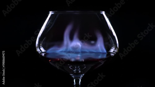 Flaming cognac drink in snifter glass over black background