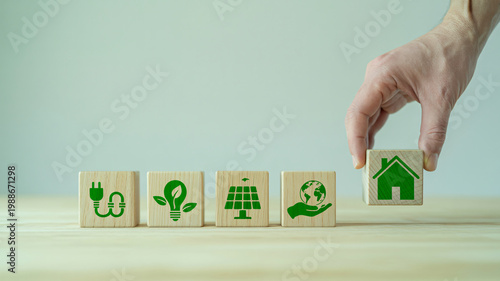 A hand placing a wooden block with a house icon on a table with eco-friendly symbols.