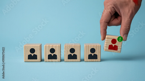 A hand placing a unique person icon among uniform icons on wooden blocks