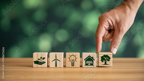 A hand placing a wooden block with a tree icon, representing eco-friendly and sustainable living concepts.