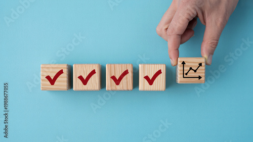 A hand placing a wooden block with a graph symbol next to blocks with checkmarks on a blue background