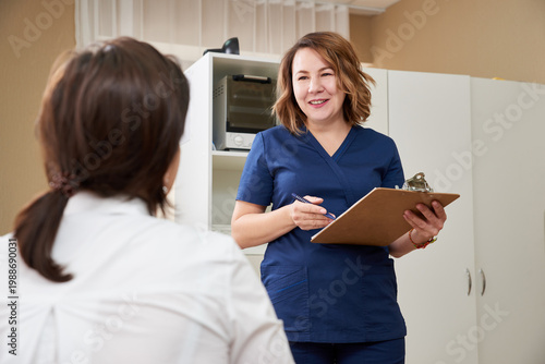 Foto doctor is talking with young female patient and making notes while standing near