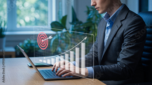 A businessman using a laptop with a virtual graph and target on the screen in a modern office