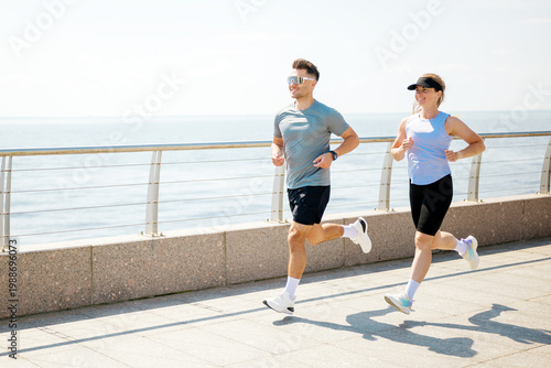 Slika na platnu Joyful runners enjoy a sunny morning jog along the beautiful waterfront promenad