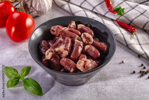 Foto Raw chicken hearts in a black bowl with fresh ingredients like tomatoes, garlic,