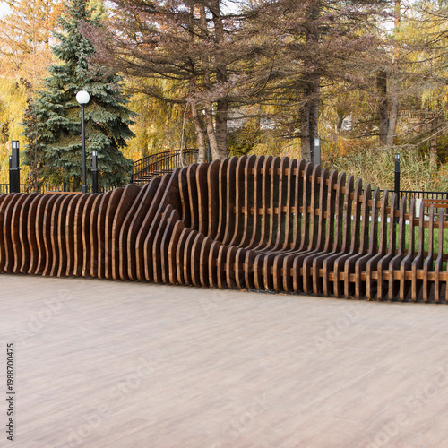 Modern sculptural wooden bench in an autumn city park