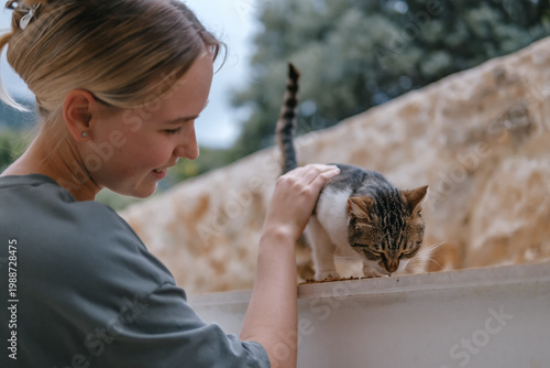 Fotografi Young woman gently pets cat outdoors, care for animals, human and pet friendship, animal friend, compassion, love for pets, domestic cat, caring owner, trust, tenderness