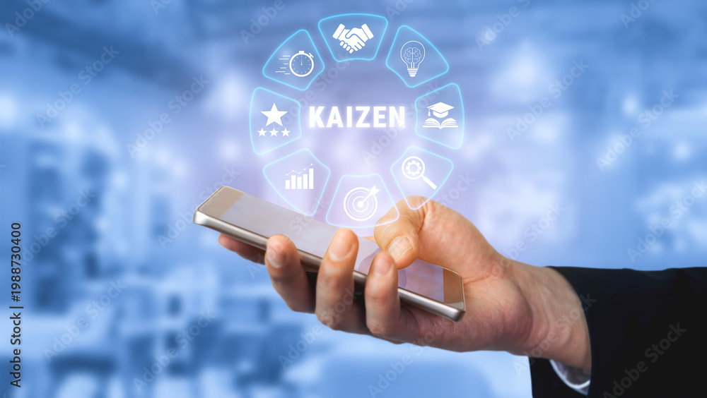 Fototapeta premium Hand Holding Smartphone Displaying Kaizen Concept with Growth Icons and Blue Background in a Modern Office Setting for Business Strategy and Improvement Quark.