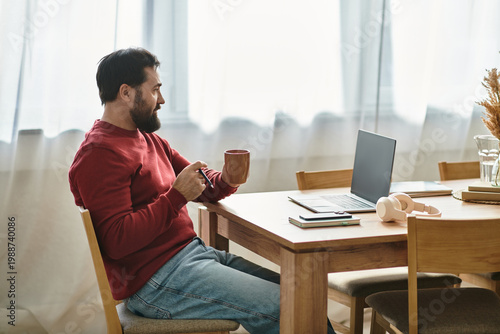 Canvas Print Relaxing at home, a handsome man enjoys coffee while working on his laptop in a