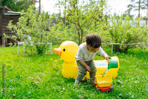 Child pouring water into toy truck beside inflatable duck tub 