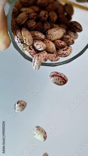 Pinto beans pouring from glass cup in slow motion close up.Dynamic shot of speckled cranberry beans falling from transparent water glass for organic food production and healthy kitchen recipes concept