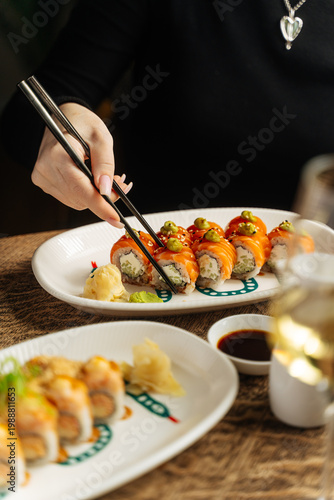 Person picking up sushi roll with chopsticks at restaurant table