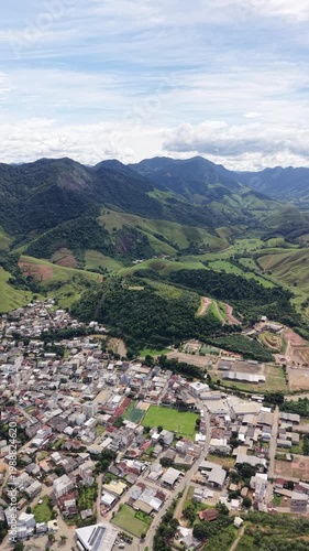 Aerial drone view of Alfredo Chaves city in Espírito Santo, Brazil. Urban area surrounded by green mountains, hills and rural landscape under blue sky, typical countryside scenery.