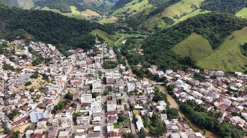 Aerial drone view of Alfredo Chaves city in Espírito Santo, Brazil. Urban area surrounded by green mountains, hills and rural landscape under blue sky, typical countryside scenery.