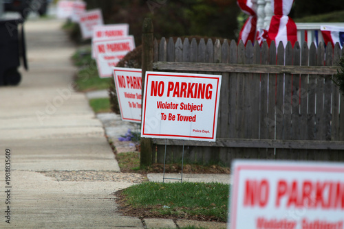 A city street lined with trees, a clear sidewalk, a row of NO PARKING signs and pedestrian 
