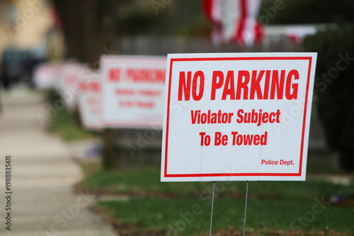 A city street lined with trees, a clear sidewalk, a row of NO PARKING signs and pedestrian 