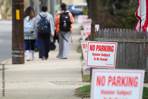 A city street lined with trees, a clear sidewalk, a row of NO PARKING signs and pedestrian 