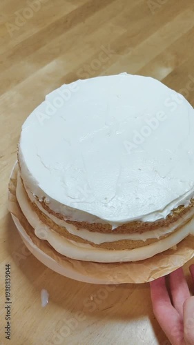 Cake rotating on a stand while a baker spreads cream frosting. Close-up of decorating process, smooth icing, professional or home pastry work, dessert preparation, bakery concept, sweet food video