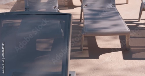 PORTOCOLOM, MALLORCA, SPAIN - OCTOBER, 2025: Midday sun creates strong contrast on empty sun loungers, shadows stretch across the resort patio creating relaxing atmosphere