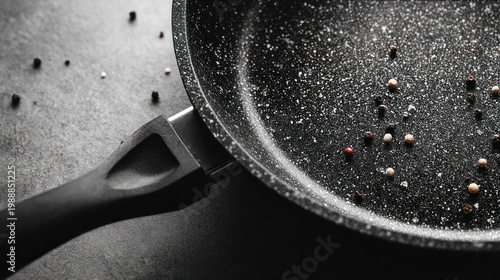 Close up of a non stick frying pan with peppercorns on dark surface