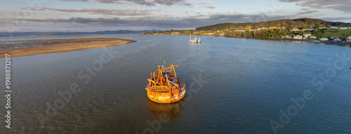 Photos A large, rusty dredging barge sits in the calm waters of the Kawhia Harbour, Kawhia, Waikato, New Zealand, at sunrise
