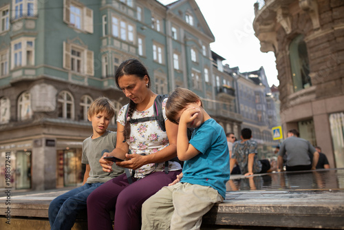 Tired Family Sits Together on the Street While Looking at a Smartphone