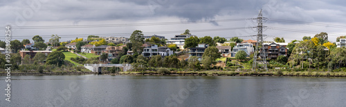 Fotografie Panoramic view of the Maribyrnong River in Ascot Vale, Melbourne, featuring waterfront houses on a lush green riverbank with a high-voltage power line tower