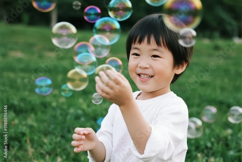 A young child smiling and reaching for floating soap bubbles in a grassy outdoor setting