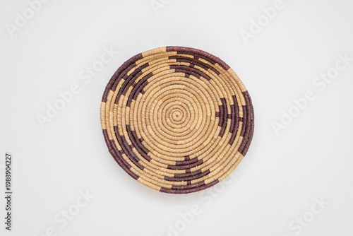 Handcrafted circular woven bowl featuring intricate geometric designs in dark purple and natural straw fibers, shown from a top-down perspective on a clean white background for versatile design