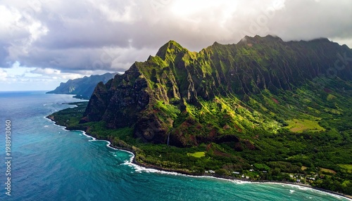 Jagged green mountains descend to meet the turquoise ocean on a cloudy day