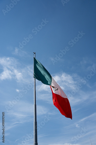 Mexican flag waving on pole against blue sky with copy space