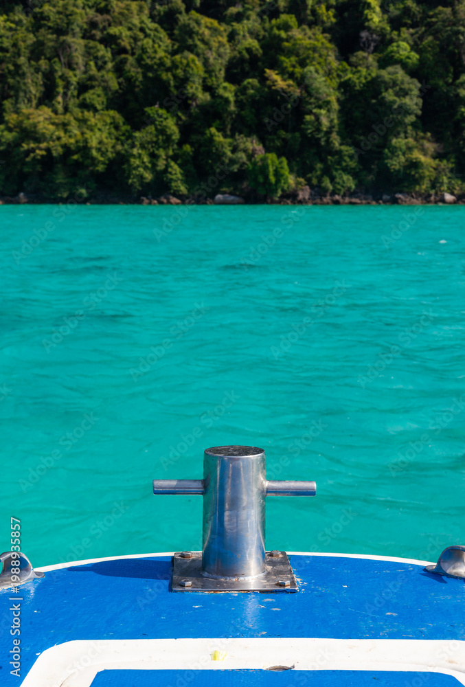 Fototapeta premium Bow bollard on boat facing tropical island. Turquoise sea in the background. Lush green forested coastline.