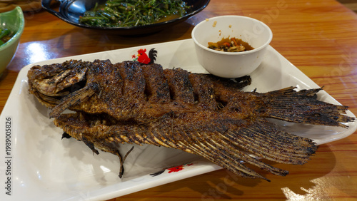 Gurame bakar madu  (Honey-Grilled Gurame Fish) : Grilled gourami fish with honey and soy sauce. Served with chili sauce on a white plate.