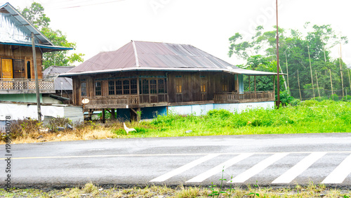 A photo of a typical stilt house from a region in Indonesia, with a large grassy yard and chickens roaming around it.