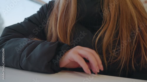 Caucasian woman at cafe counter, poised hand on tabletop, winter jacket with hood, long red hair, neutral expression, subtle furtive motion suggesting snatcher, ambient daylight through window,