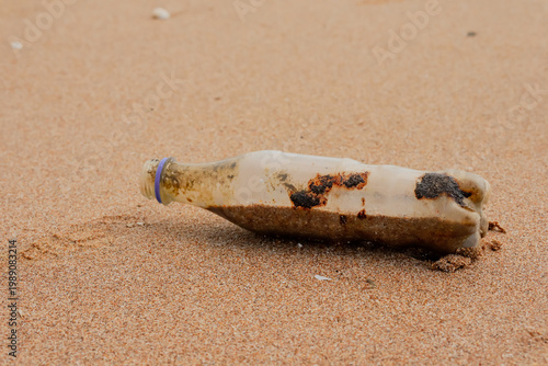 Photos An old plastic bottle covered in dirt and oil residues washed ashore on a sandy beach
