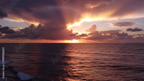 Sunrise over calm ocean waves with cloudy sky and sun rays shining through