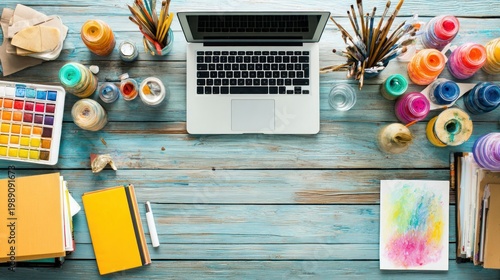Colorful art supplies and a modern laptop arranged on a rustic wooden desk surface