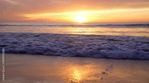 Sunset over calm ocean waves gently lapping at the serene beach shore with footprints