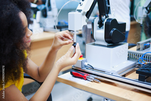 Canvastavla Young man meticulously assembles a robotic arm component on a workbench in a dimly lit workshop, demonstrating STEM education with focused intensity and wearing a yellow shirt