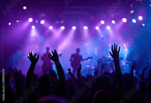 Concert crowd with hands raised in excitement under purple stage lights.