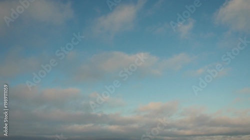 Clouds drift through the sky in a time lapse showing how they change during the late afternoon. This happens over a wooded area with trees in the background.