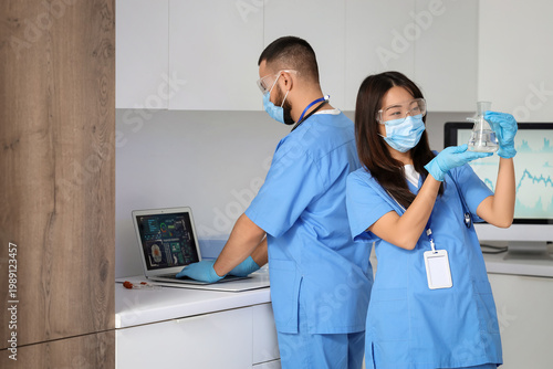 Young doctors with laptop and flask analyzing scientific data in laboratory