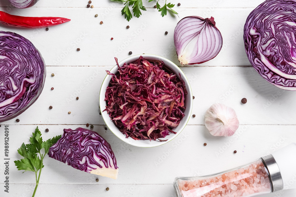 Obraz premium Bowl of tasty red sauerkraut with peppercorns, onion, garlic, parsley and sea salt on white wooden background