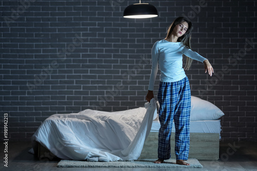 Foto Female sleepwalker with blanket near bed against black brick wall in dark bedroo