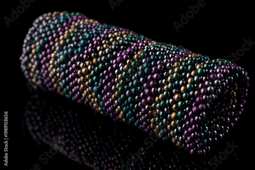 Colorful beaded cylindrical ornament with intricate patterns and reflective surface on black.