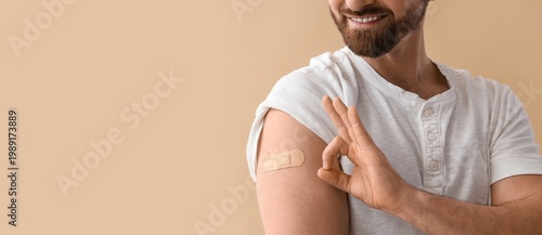 Man with applied medical patch showing OK after vaccination on beige backgrou...