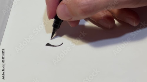 Close up of hand holding black calligraphy pen over blank white paper and drawing a line