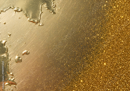 Golden liquid with glittering particles on a metallic surface with a smooth and rough texture