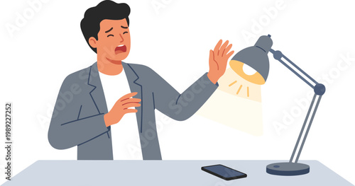 A man sits at a desk gesturing with a lamp and phone nearby.